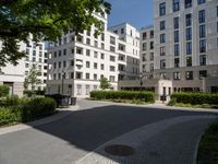 a wide paved street surrounded by tall white building facades surrounded by greenery and bushes