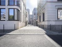 a person walks through an empty courtyard lined with tall buildings as the sun shines on a stone road