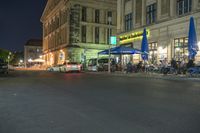 cars parked outside an outdoor restaurant at night with people dining outside the building and tables lined up in front of it