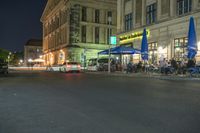 cars parked outside an outdoor restaurant at night with people dining outside the building and tables lined up in front of it