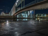 a reflection on a pavement near a bridge by a river at night in city, with a clock tower on the other side