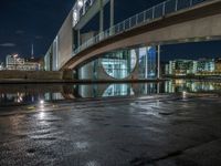 a reflection on a pavement near a bridge by a river at night in city, with a clock tower on the other side