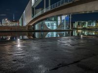 a reflection on a pavement near a bridge by a river at night in city, with a clock tower on the other side