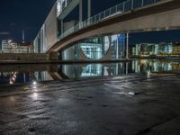 a reflection on a pavement near a bridge by a river at night in city, with a clock tower on the other side