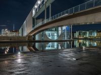 a reflection on a pavement near a bridge by a river at night in city, with a clock tower on the other side