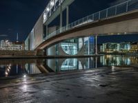 a reflection on a pavement near a bridge by a river at night in city, with a clock tower on the other side