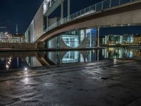 a reflection on a pavement near a bridge by a river at night in city, with a clock tower on the other side