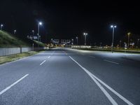 an empty road surrounded by a concrete wall and light posts on a mountain side at night