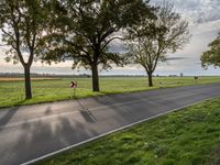 a paved road with a grassy field next to trees and a path through it near the fields