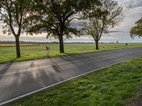 a paved road with a grassy field next to trees and a path through it near the fields