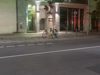 an empty street and parked bikes on a pole in front of a building with green lights