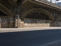 graffiti covered brick wall and gate under an overpass in an urban area with sun light