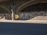 graffiti covered brick wall and gate under an overpass in an urban area with sun light