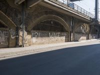 graffiti covered brick wall and gate under an overpass in an urban area with sun light