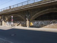 graffiti covered brick wall and gate under an overpass in an urban area with sun light