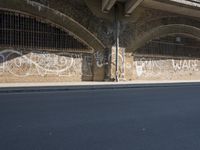 graffiti covered brick wall and gate under an overpass in an urban area with sun light