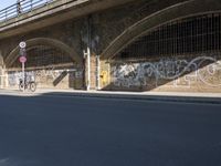 graffiti covered brick wall and gate under an overpass in an urban area with sun light