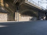 graffiti covered brick wall and gate under an overpass in an urban area with sun light