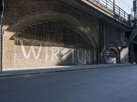 graffiti covered brick wall and gate under an overpass in an urban area with sun light