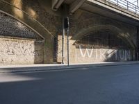 graffiti covered brick wall and gate under an overpass in an urban area with sun light