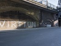 graffiti covered brick wall and gate under an overpass in an urban area with sun light