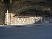 graffiti covered brick wall and gate under an overpass in an urban area with sun light