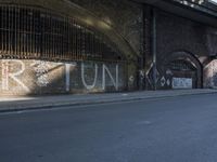 graffiti covered brick wall and gate under an overpass in an urban area with sun light