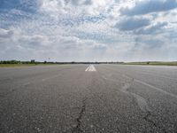 an airport runway with empty roadway and clouds overhead on blue and grey sky day, with plane taking off from the airport