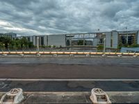 two concrete barriers on a roadway under a cloudy sky with buildings in the background and an empty street