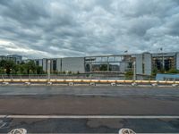two concrete barriers on a roadway under a cloudy sky with buildings in the background and an empty street