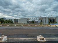 two concrete barriers on a roadway under a cloudy sky with buildings in the background and an empty street