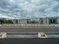 two concrete barriers on a roadway under a cloudy sky with buildings in the background and an empty street