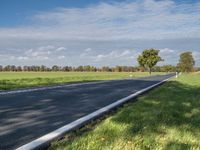 a road with an empty roadway surrounded by green grass and trees under a clear blue sky