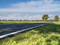 a road with an empty roadway surrounded by green grass and trees under a clear blue sky