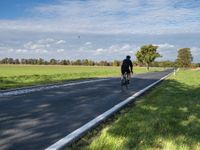 a road with an empty roadway surrounded by green grass and trees under a clear blue sky