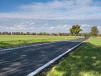 a road with an empty roadway surrounded by green grass and trees under a clear blue sky