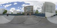 a fish eye lens of skateboarders riding the ramp at a skate park with tall buildings in the background