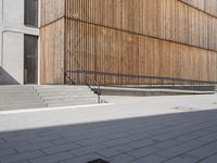 a skateboarder riding down the sidewalk near some steps and a wooden building with a metal railing