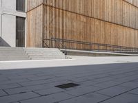 a skateboarder riding down the sidewalk near some steps and a wooden building with a metal railing