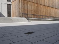 a skateboarder riding down the sidewalk near some steps and a wooden building with a metal railing