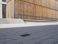 a skateboarder riding down the sidewalk near some steps and a wooden building with a metal railing