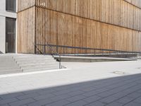 a skateboarder riding down the sidewalk near some steps and a wooden building with a metal railing