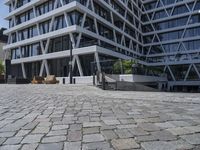 a stone courtyard sits between two office buildings with a glass fronted front entrance and patio area