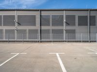 an empty parking lot with some benches next to the large building on the right side