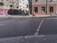 a city street with several people walking on it and buildings in the background, there's a traffic light on one side, a man is walking down one side,