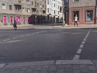 a city street with several people walking on it and buildings in the background, there's a traffic light on one side, a man is walking down one side,