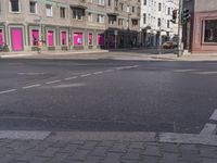 a city street with several people walking on it and buildings in the background, there's a traffic light on one side, a man is walking down one side,