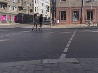 a city street with several people walking on it and buildings in the background, there's a traffic light on one side, a man is walking down one side,