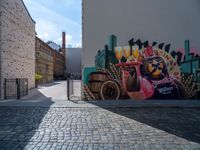 a street art mural with horse drawn carriage in the center of it, and a brick road leading to a building