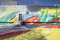 colorful mural painted on the wall of a building near a playground and park area with children playing outside